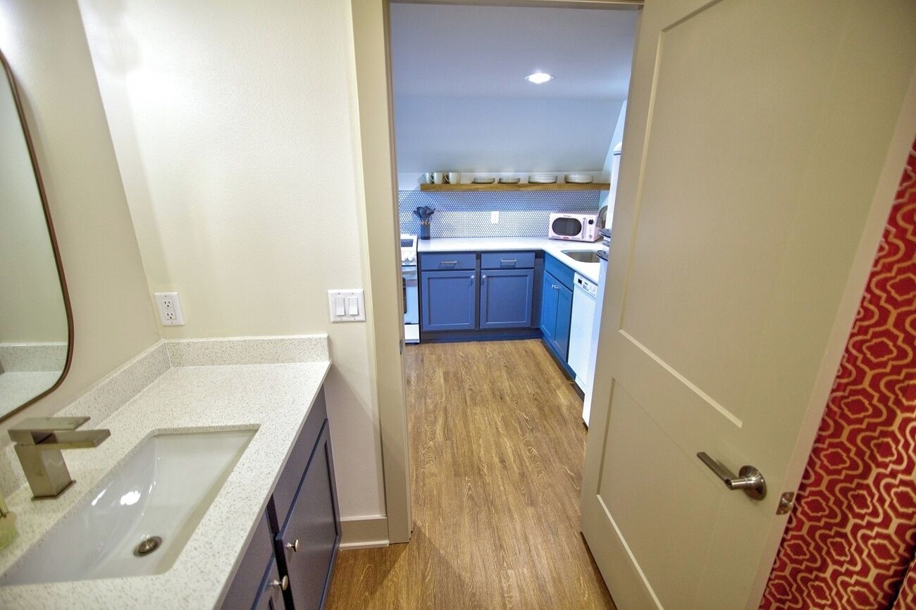 A narrow hallway leading to a bathroom and a kitchen area with blue cabinets and a microwave.