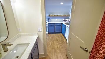 A narrow hallway leading to a bathroom and a kitchen area with blue cabinets and a microwave.