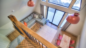 Un salon moderne avec un canapé, une petite table et des chaises. Il y a de grandes fenêtres et un escalier.
