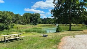 Une table de pique-nique et un petit étang se trouvent dans un espace verdoyant, avec des arbres en arrière-plan.