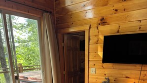 Habitació d'una cabana de fusta amb un llit, una televisió penjada a la paret i vista a l'exterior.