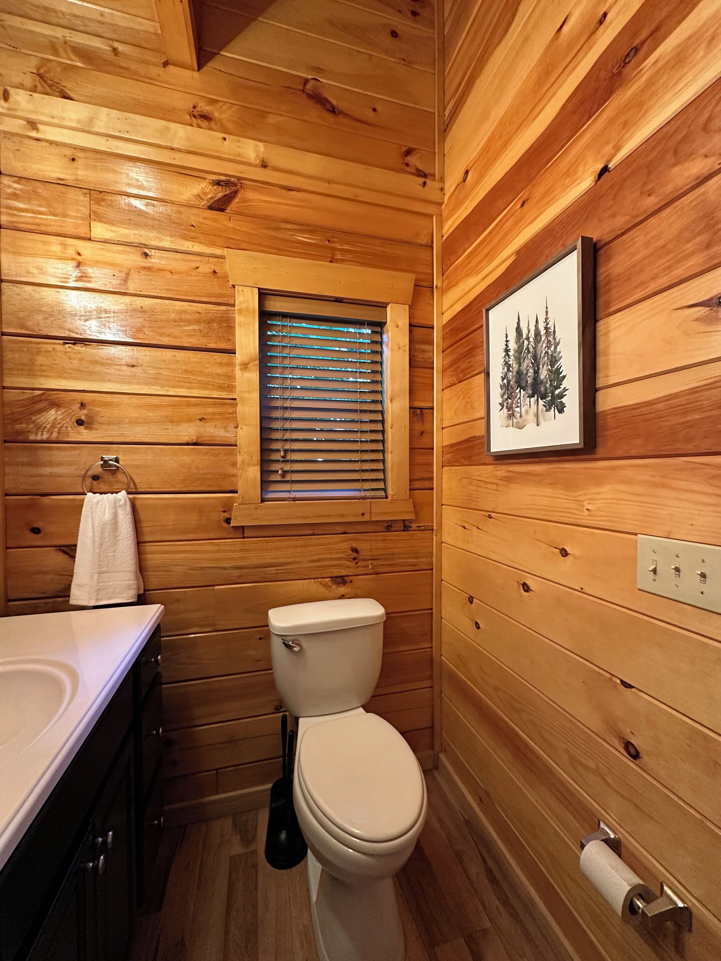 Een houten badkamer in een vakantiehuisje, met toilet, wastafel en raam.