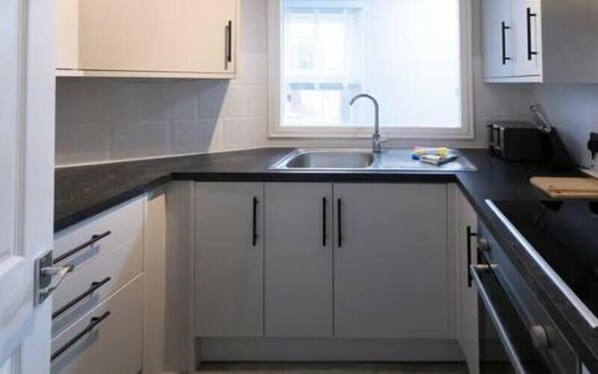 A compact kitchen with white cabinets, a black countertop, and a window above the sink.