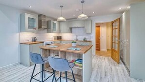 A modern kitchen with a central island, bar stools, pendant lighting, and a view into the adjacent dining area. - Middlecroft Annex by Guestz (Sutton)