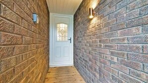 A narrow hallway with brick walls and a wooden floor, leading to a white door with a glass panel. - Middlecroft Annex by Guestz (Sutton)