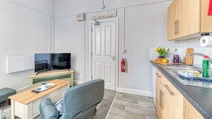 A compact living space with a television, a sofa, a dining table, and a kitchen area with a sink and cabinets.