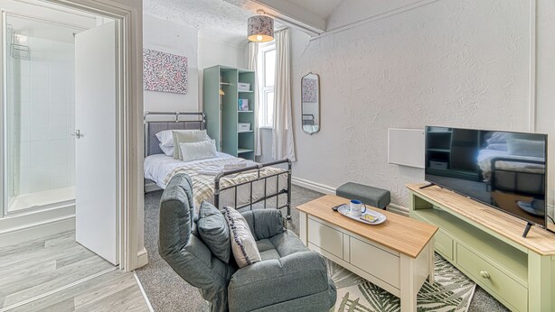 A modern bedroom with a bed, a TV, a desk, and a green shelving unit.
