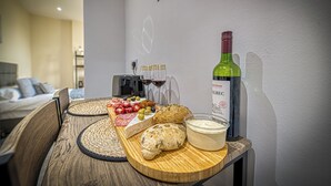 Ein Holztisch mit Käseplatte, Oliven, Brot und einer Weinflasche in einem Zimmer mit einem Bett und einer Wand mit dem Schriftzug 'HAPPY DAY'.