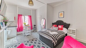 Ein Schlafzimmer mit Bett, Schreibtisch, Stuhl, Spiegel und einem Fenster mit Vorhängen.