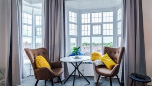 A room with two brown leather chairs, a small round table with a potted plant, and a view through large windows. - Chester Heights by Guestz (Chester)