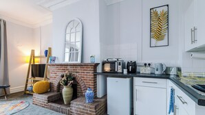 A compact kitchen with a brick fireplace, white cabinetry, and a small refrigerator. - Chester Heights by Guestz (Chester)