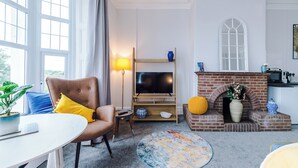 A living room with a television, a brick fireplace, a dining table, and a large window. - Chester Heights by Guestz (Chester)
