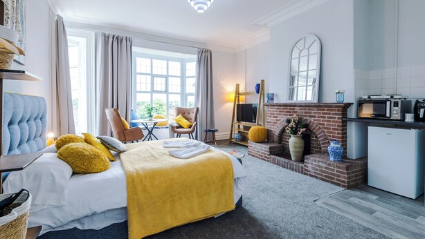 A hotel room with a bed, a chair, a table, a fireplace, and a kitchenette. - Chester Heights by Guestz (Chester)