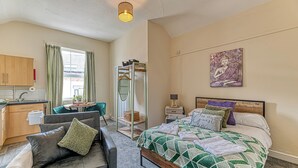A bedroom with a bed, a bedside table, a nightstand, a chair, a sofa, a wardrobe, and a window with curtains.