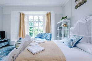 Une chambre à coucher avec un grand lit, une télévision, une armoire et une fenêtre avec des rideaux.