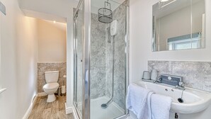 A modern bathroom with a glass-enclosed shower, a white toilet, and a sink with a mirror above. - Chester Heights by Guestz (Chester)