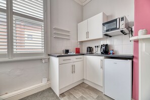 A compact kitchen with white cabinets, a microwave, a coffee maker, and a small refrigerator.