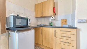 Una cocina con microondas, refrigerador, armarios de madera y un lavamanos.