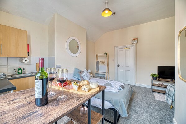 A compact hotel room with a kitchenette, a dining area, a bed, and a television.
