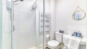 A bathroom with a glass shower enclosure, white tiles, a toilet, and a sink with a towel. - Chester Heights by Guestz (Chester)