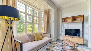 A modern living room with a sofa, a floor lamp, a TV, and a patterned rug. - Chester Heights by Guestz (Chester)