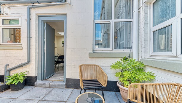 A patio with wicker furniture, a potted plant, and a door leading to an interior space. - Chester Heights by Guestz (Chester)