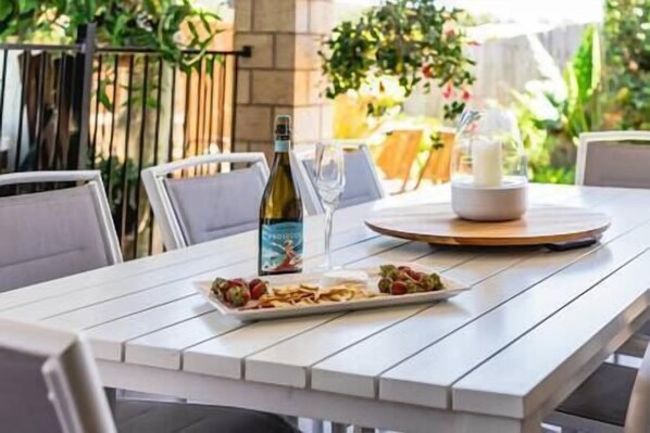 A white table with a plate of food, a bottle of wine, and a glass of wine.