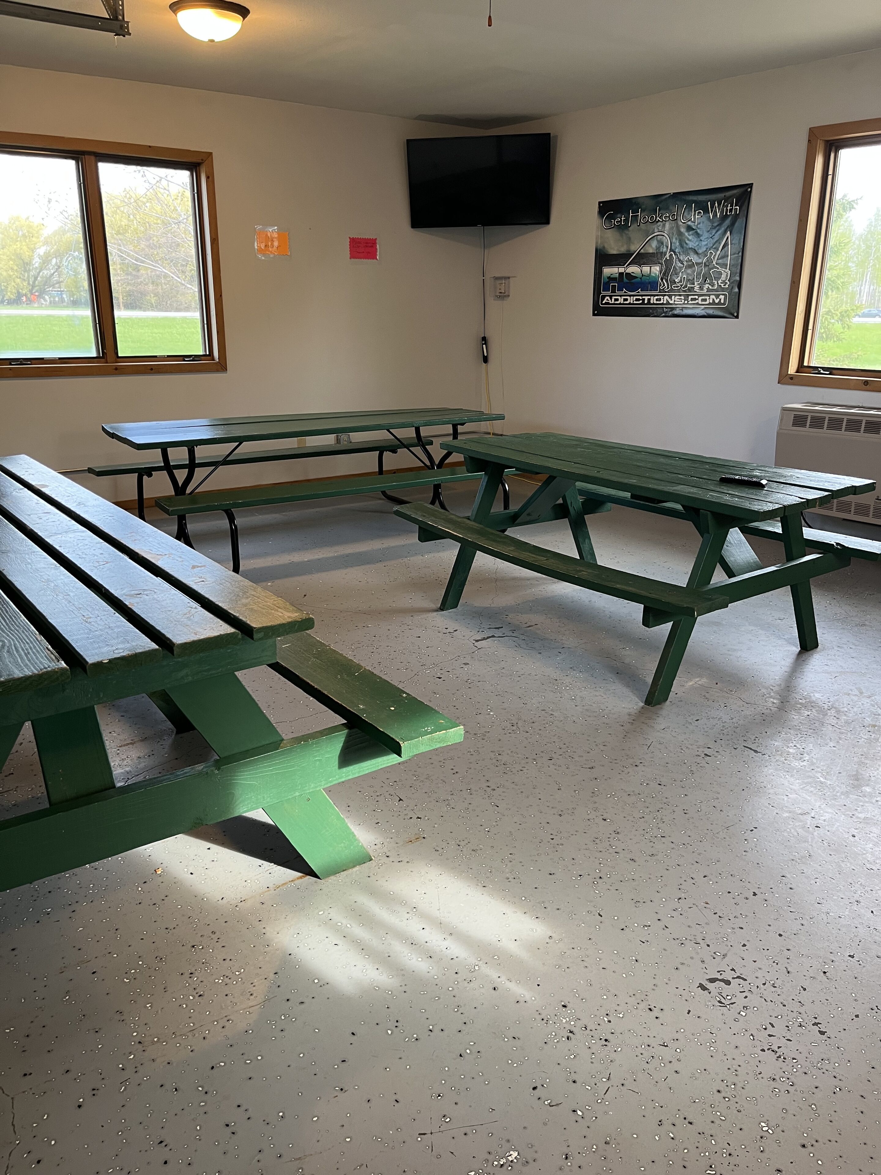 A room with picnic tables, a television mounted on the wall, and a window with a view of greenery.