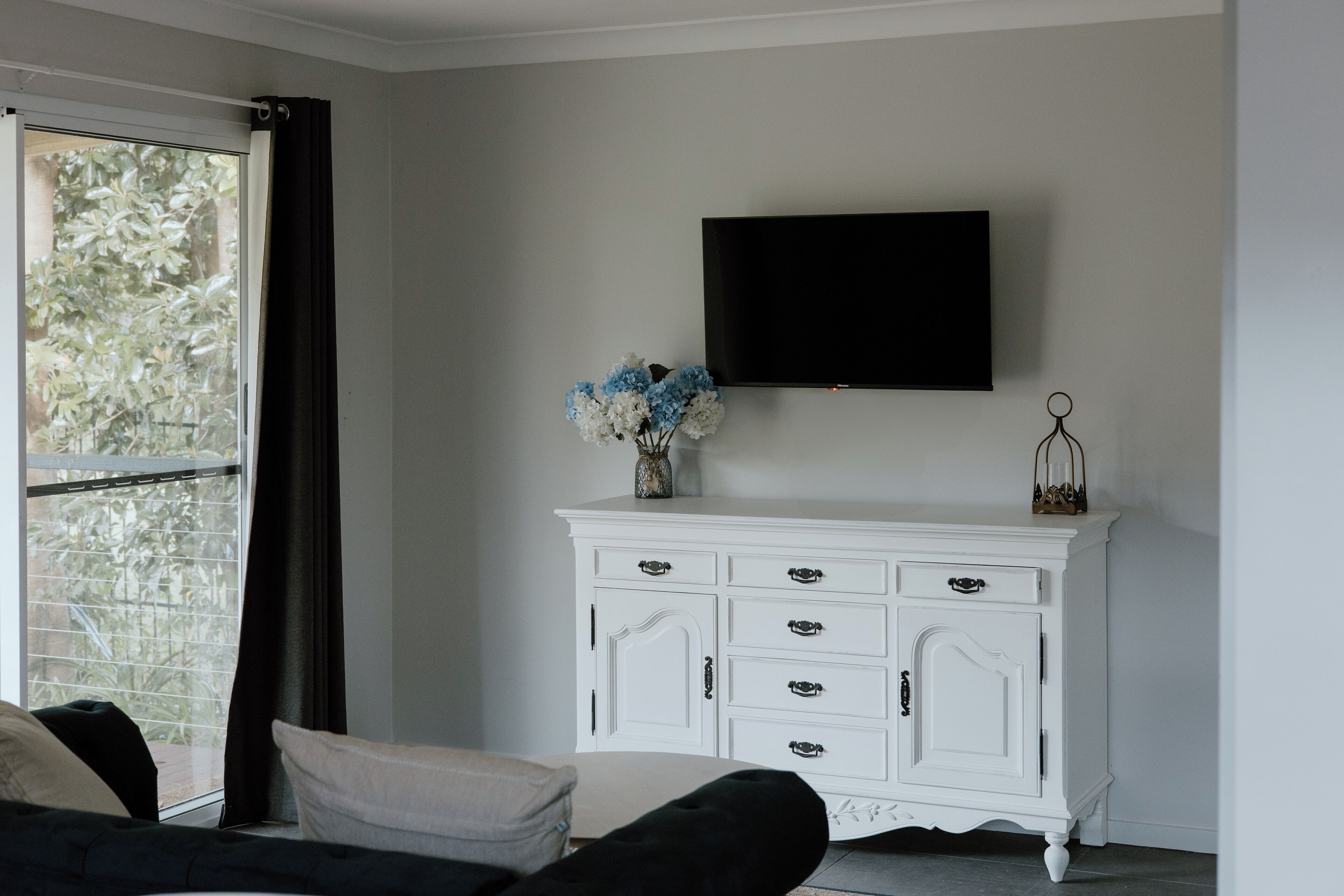 A living room with a white cabinet, a flat-screen TV, and a window with curtains.