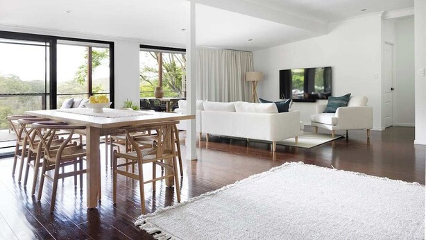 A modern living room with a dining area, white furniture, and a large window offering a view of greenery. - Luxury Hinterland Hideaway with Breathtaking Views (Queensland)