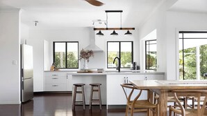 A modern kitchen with white cabinetry, a wooden dining table, and bar stools. - Luxury Hinterland Hideaway with Breathtaking Views (Queensland)
