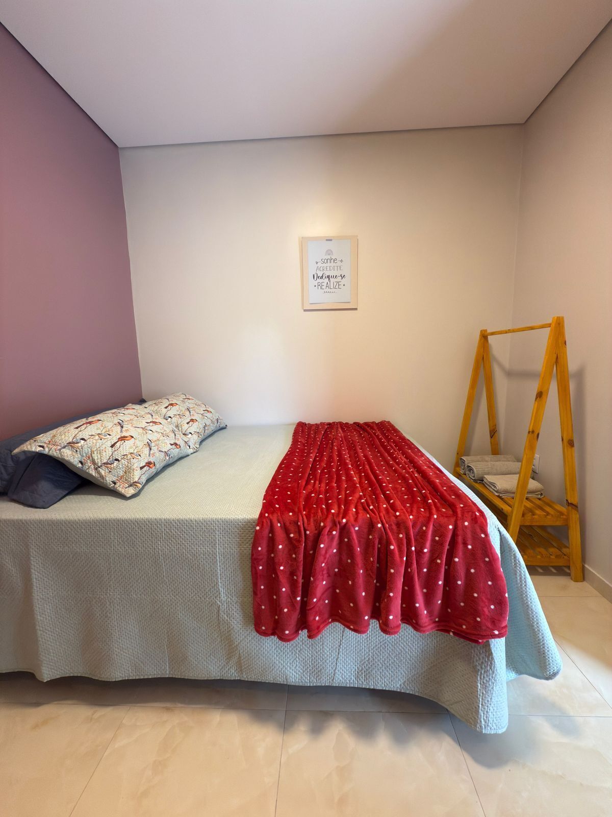 Een slaapkamer met een bed, een kussen, een rood stippenkleurig plaid, een houten ladder en een inspirerende quote op de muur.