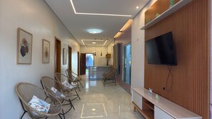 Un hall d’hôtel moderne avec un long couloir, des fauteuils en osier, un téléviseur à écran plat et un mur décoratif en bois.