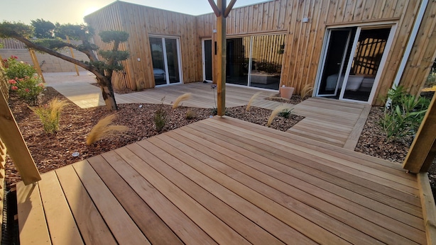 Una terraza de madera con una pérgola, rodeada de plantas en macetas y un pequeño jardín.