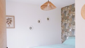 Un dormitorio con cama, lámpara colgante, pared con papel tapiz estampado y una puerta.