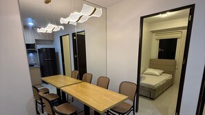 A modern dining area with a wooden table and chairs, a decorative ceiling light, and a view into a bedroom through an open doorway.