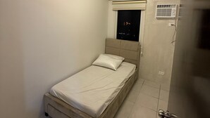 A small, neatly arranged bedroom with a single bed, a window with a night view, and an air conditioning unit on the wall.