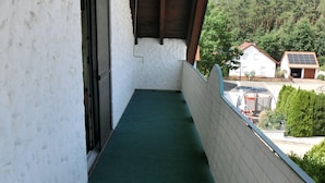 Un balcón estrecho con alfombra verde, paredes blancas y techo de madera.