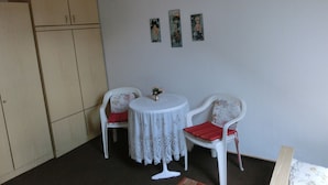 Una habitación con techo de madera, una mesa blanca con mantel de encaje, dos sillas blancas con cojines rojos y un armario de madera.