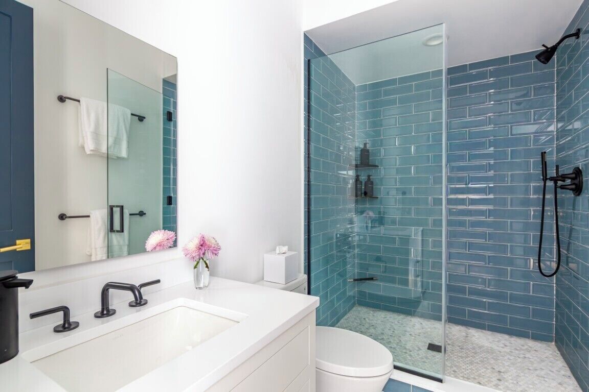 A modern bathroom with a white sink, a glass shower enclosure, and blue-tiled walls.