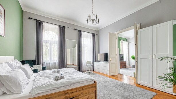 A bedroom with a wooden bed, a grey carpet, a white dresser, and a TV.