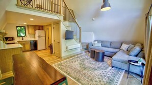 Un vaste espace de vie comprenant une table à manger en bois, un canapé gris, un tapis à motifs et un escalier menant à un niveau supérieur.