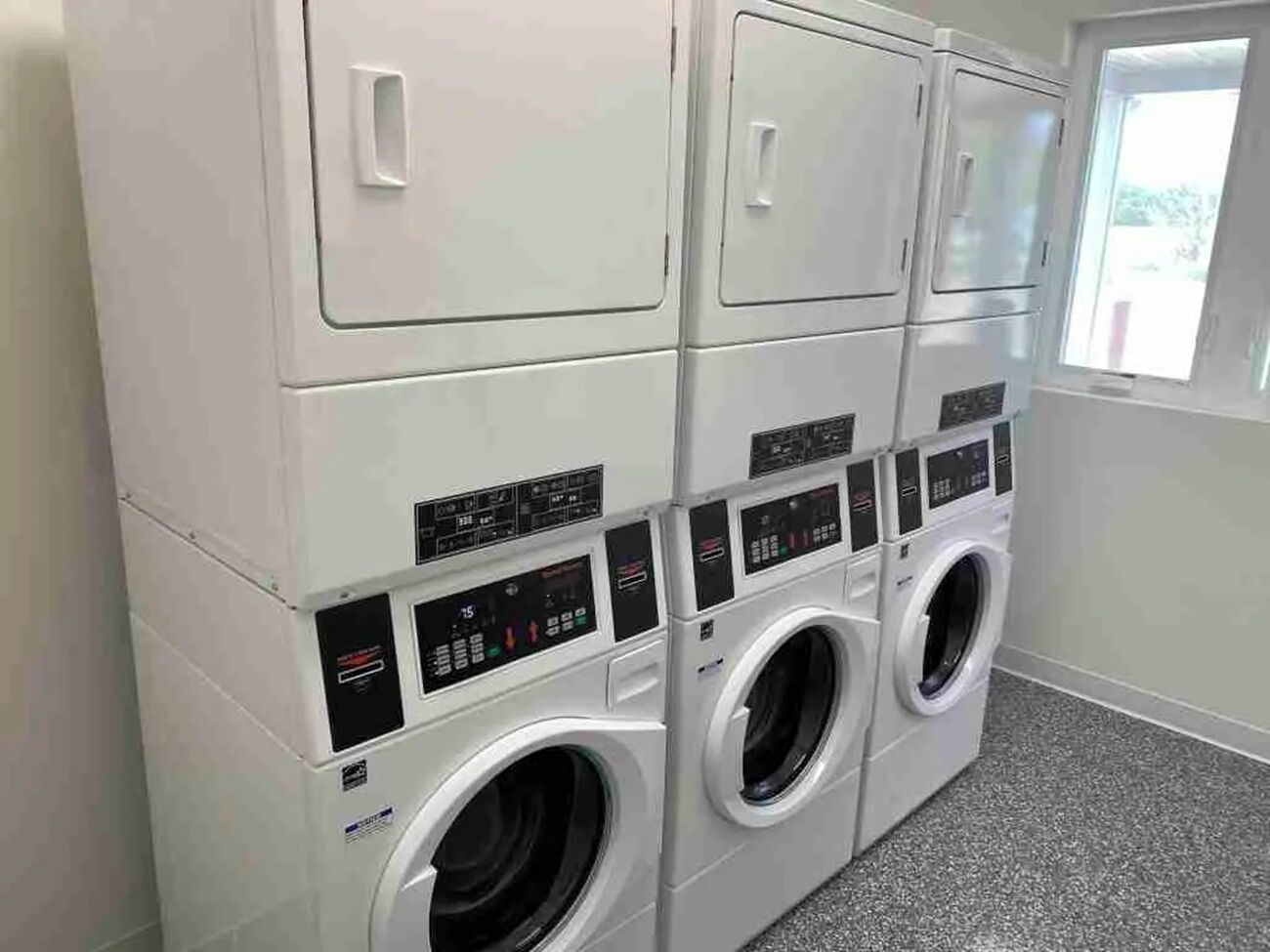 Une rangée de machines à laver blanches, fixées au mur, avec leurs panneaux de commande, et deux machines à laver à chargement frontal.