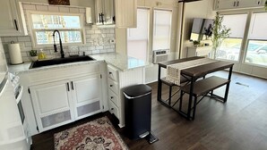 Una cocina moderna con armarios blancos, un cubo de basura negro, una mesa de comedor de madera y una alfombra estampada.