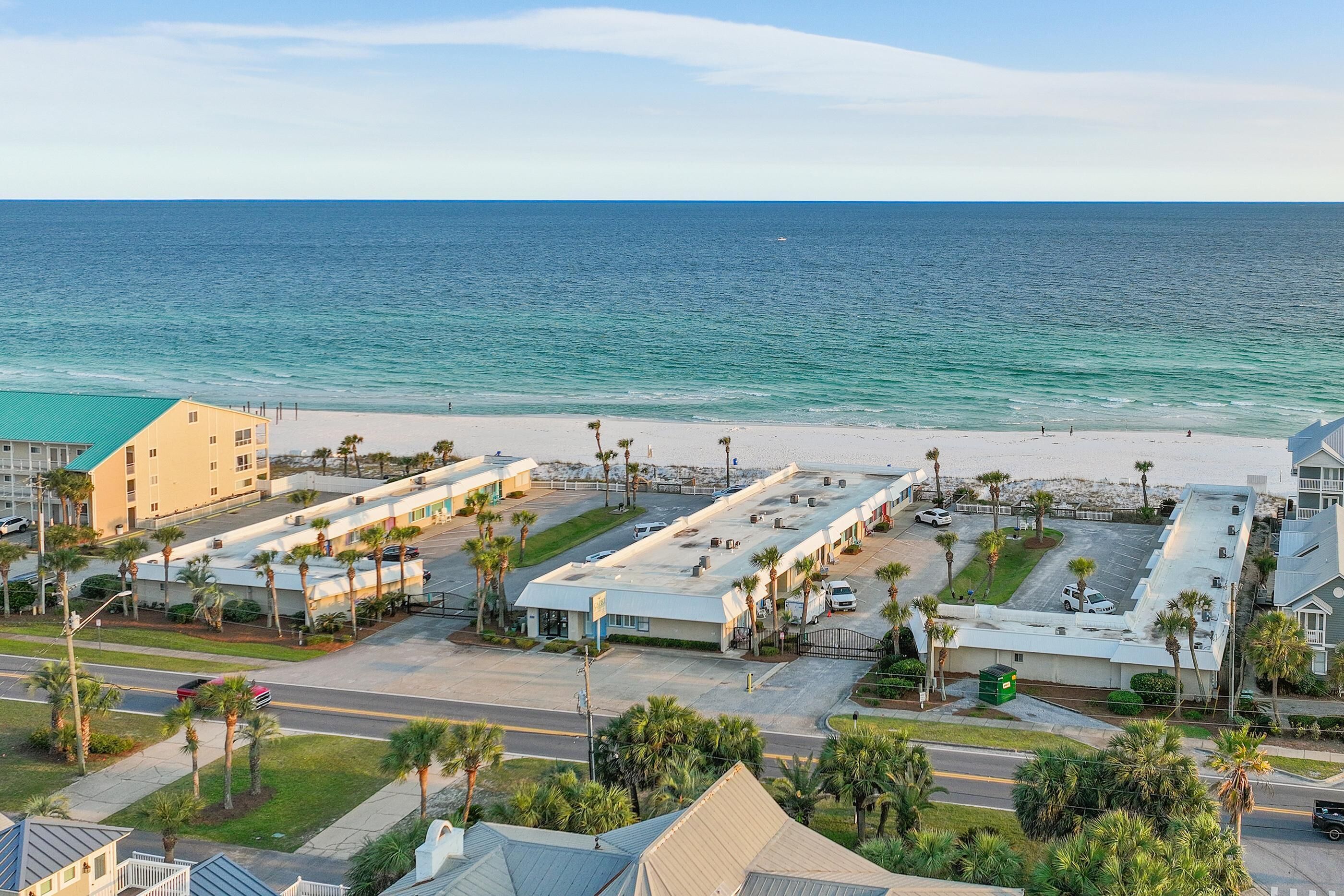 A coastal hotel with a parking lot, beach access, and palm trees.