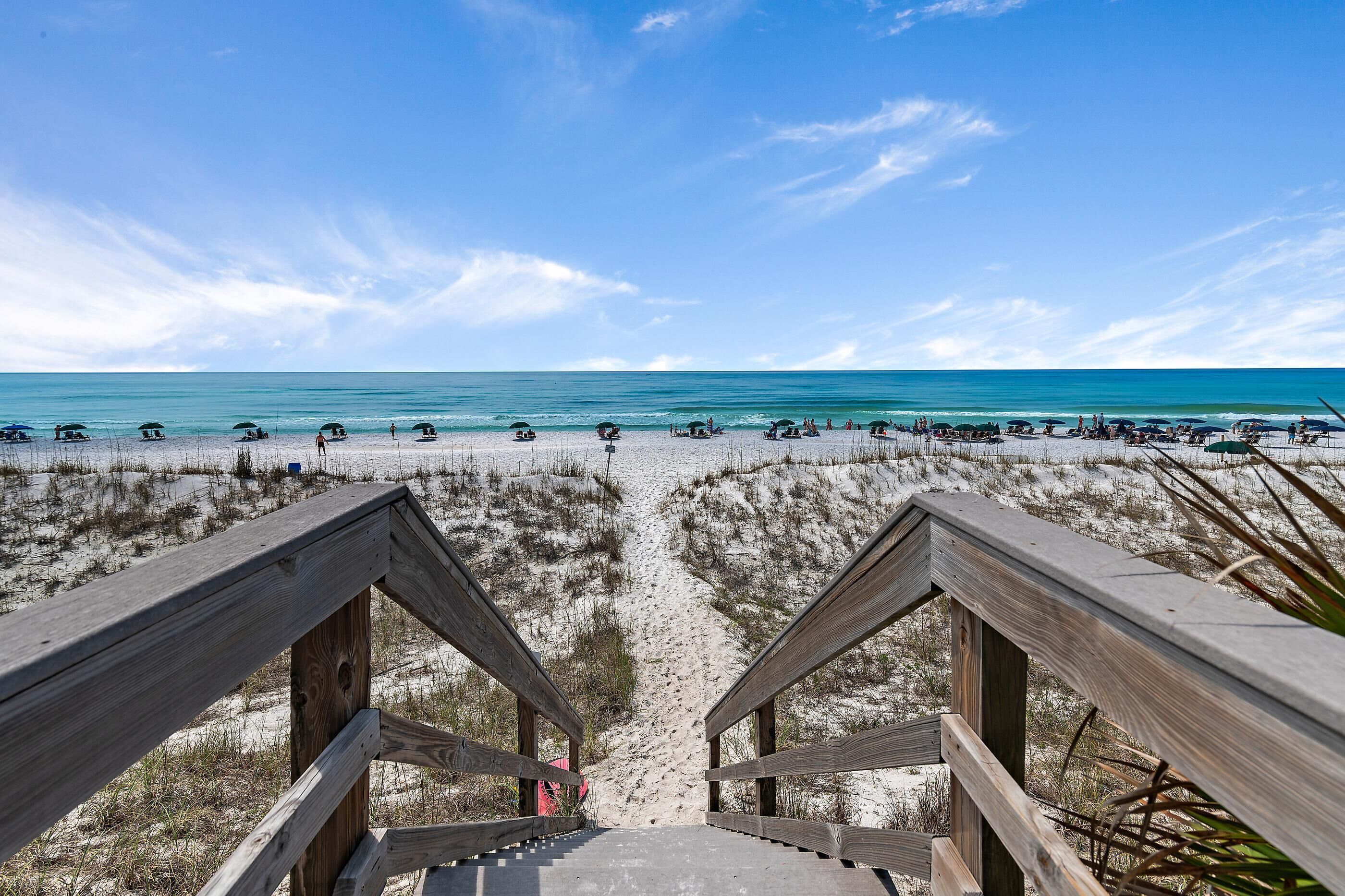 A wooden staircase leading to a beach with clear skies and calm waters.