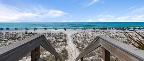 A wooden staircase leading to a beach with clear skies and calm waters.