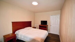 Un dormitorio con una cama individual, una mesita de noche, un televisor sobre un mueble y una puerta.