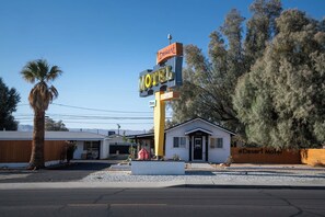 Un motel con un letrero llamativo, una piscina y un pequeño edificio con garaje.