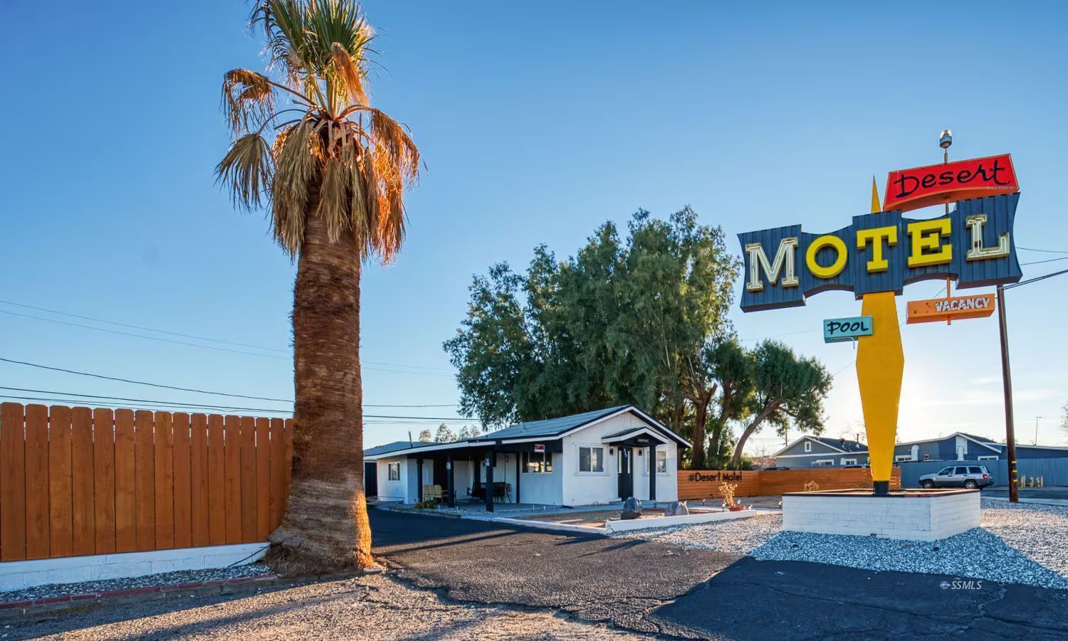 Un motel con una palmera, una piscina y un cartel que indica habitaciones disponibles.